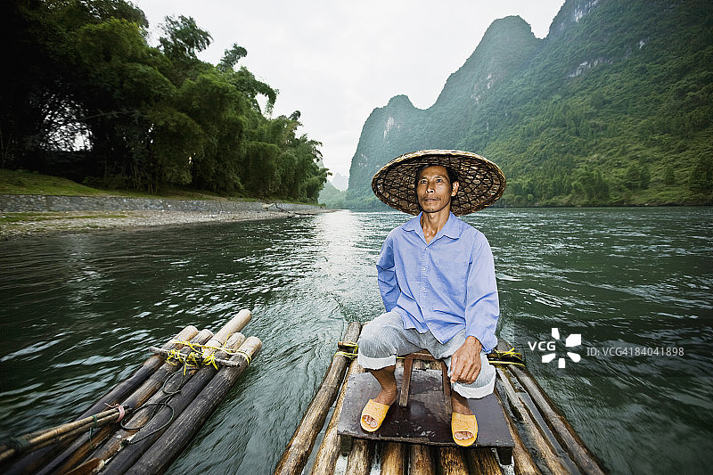 中年男人坐在木筏上，背景是桂林兴坪阳朔的山景，广西图片素材