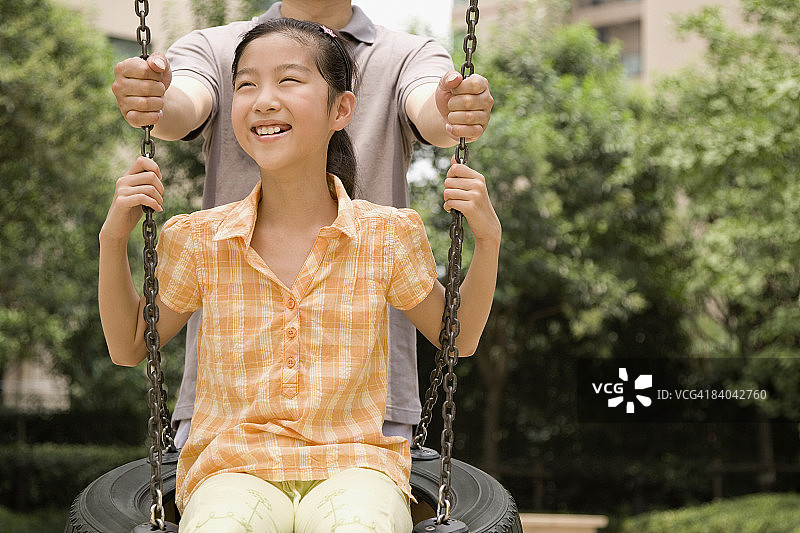 女孩荡轮胎秋千，父亲在身后陪伴图片素材