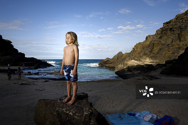 夏威夷海滩上闭着眼睛站在岩石上的小男孩图片素材