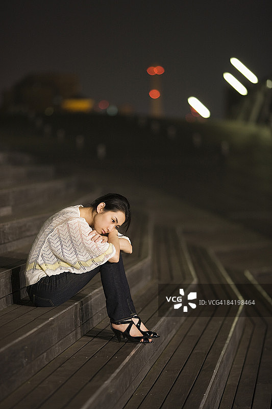 日本神奈川县横滨市夜晚坐在台阶上的年轻女人侧影图片素材
