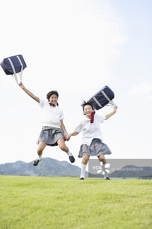 手牵手跳跃的年轻女学生图片素材