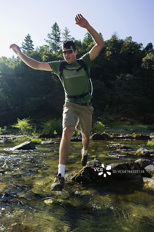 男子在岩石上跳过河流图片素材