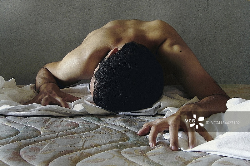 年轻男子从地板上爬到床上。图片素材
