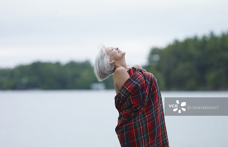 在湖边裹着毯子的女人，抬着头图片素材