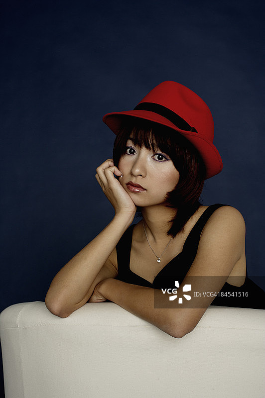 身穿黑色连衣裙、戴着红色帽子的女人背靠沙发，在工作室拍摄图片素材