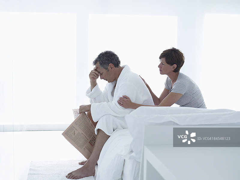 沮丧的男人拿着报纸坐在床上图片素材