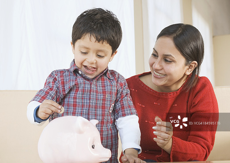 男孩和妈妈一起把硬币放进储蓄罐图片素材