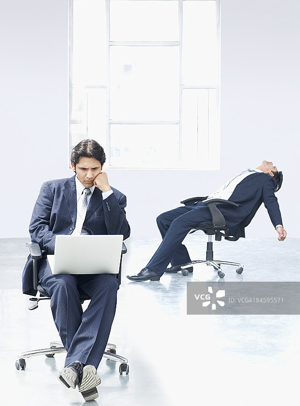 在办公室里用笔记本电脑的商人，另一位商人躺在椅子上图片素材