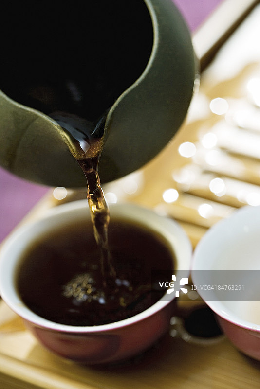 竹制茶盘上从茶壶倒入杯中的红茶图片素材