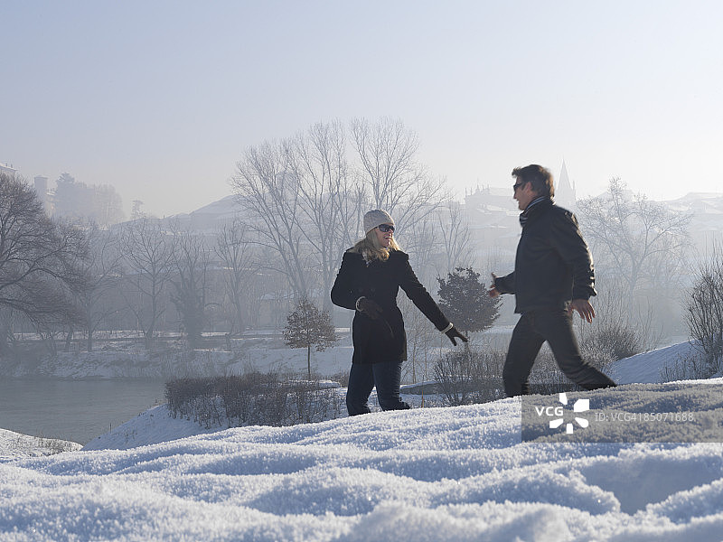 情侣在河岸的雪地里奔跑图片素材