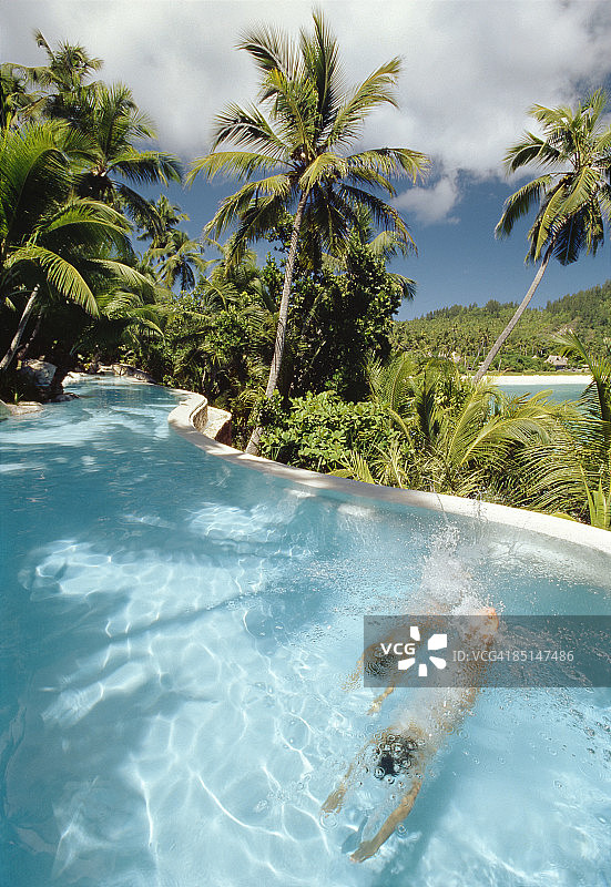 两个孩子在椰子树下的泳池里游泳图片素材