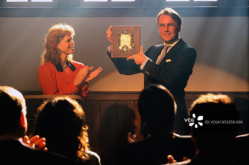 男人举起奖杯，观众在前方鼓掌图片素材