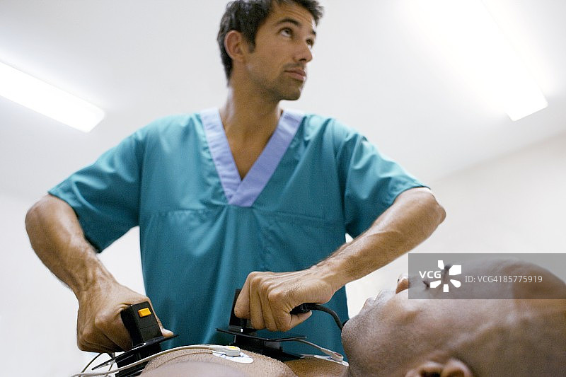 医生手持除颤器对男性患者进行胸部除颤图片素材