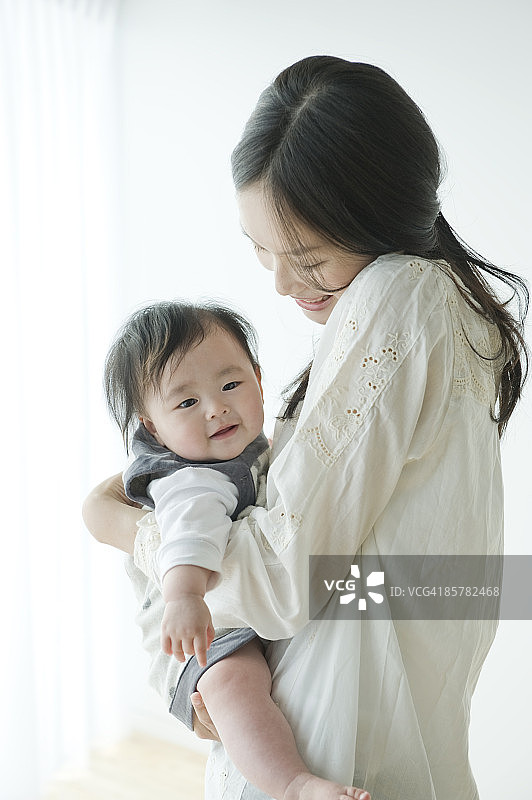 母亲抱着女婴，面带微笑，侧面视角图片素材