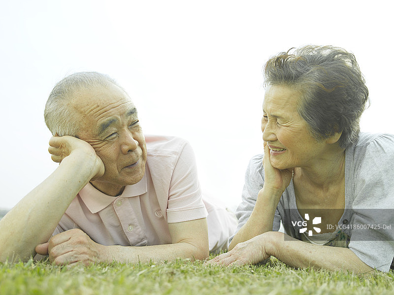 年长夫妇躺在草地上，面带微笑，彼此对视图片素材