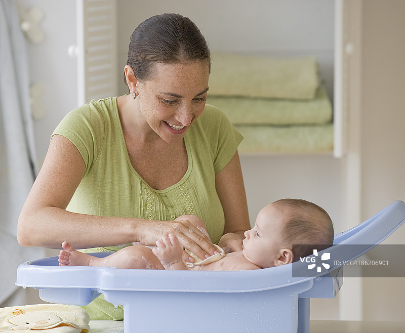 母亲在婴儿浴缸里给男婴洗澡图片素材