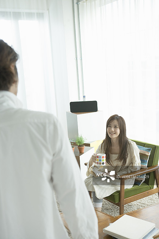 年轻女子在扶手椅上喝咖啡，面带微笑图片素材