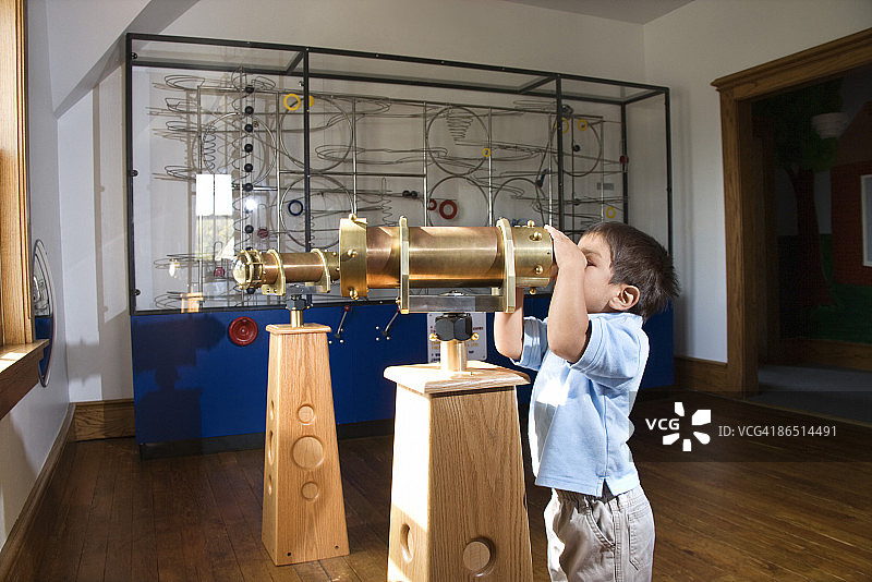 男孩在博物馆里用望远镜观察图片素材