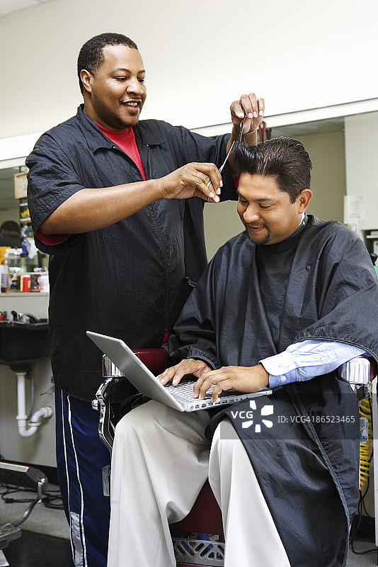 男人理发时使用笔记本电脑图片素材