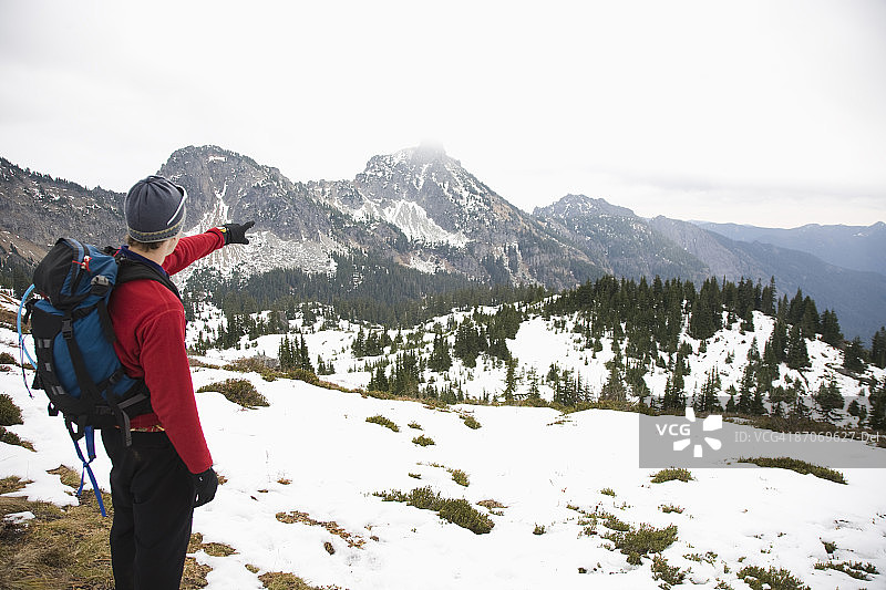在华盛顿州喀斯喀特山脉，一个男人指向远处被白雪覆盖的山峰图片素材