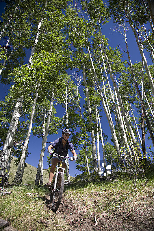 犹他州蒙蒂塞洛附近阿巴霍山脉的白杨树林中骑山地自行车的女人图片素材