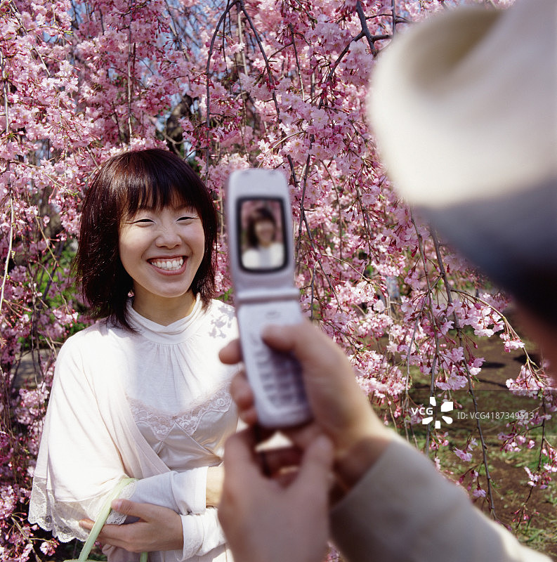一位亚洲女子在樱花树前拍照图片素材
