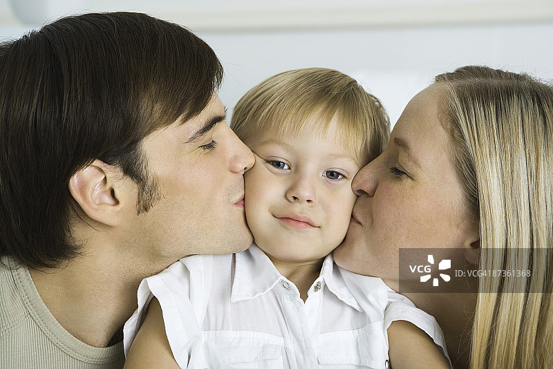 父母亲吻小男孩的脸颊，男孩看着镜头图片素材