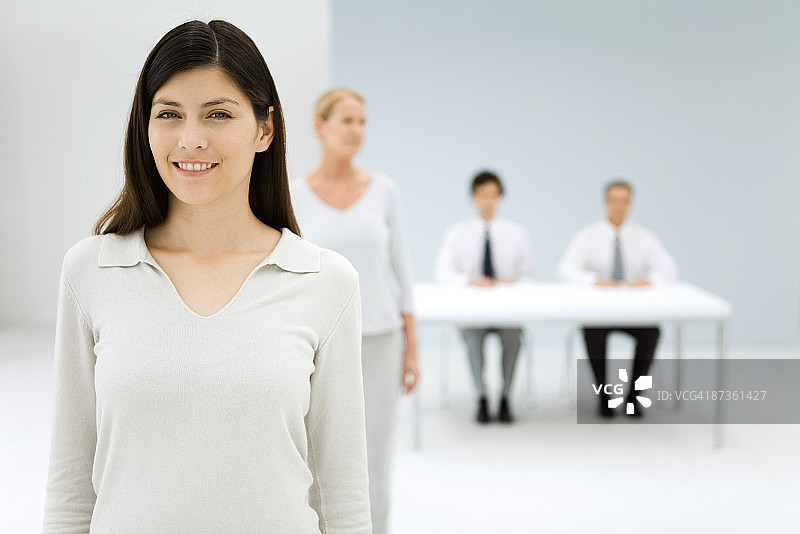对着镜头微笑的职业女性，同事在背景中图片素材
