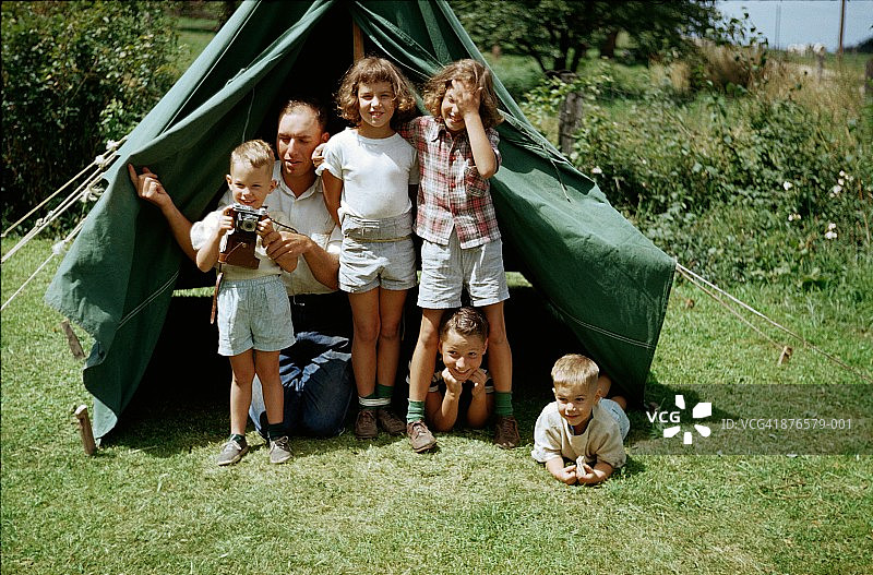 在帐篷旁玩耍的兄弟姐妹，男人给男孩（3-5岁）展示相机，1952年图片素材