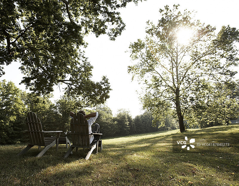 男人坐在木椅上，树后阳光图片素材