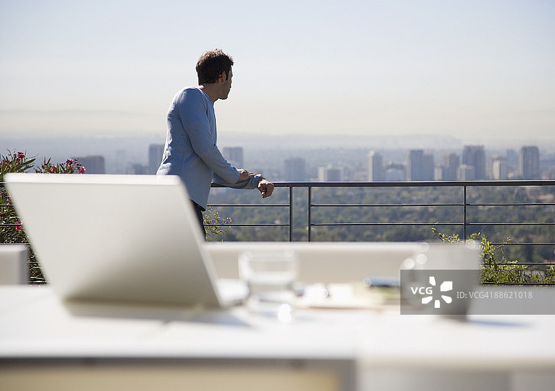 男人在阳台上俯瞰城市使用笔记本电脑图片素材