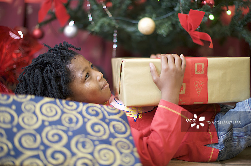 男孩躺在圣诞树前，手拿礼物（南非，夸祖鲁-纳塔尔省，彼得马里茨堡）图片素材