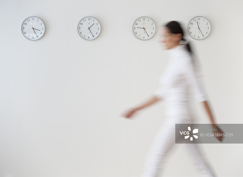 行走在时钟墙边的商务女人，动态模糊图片素材