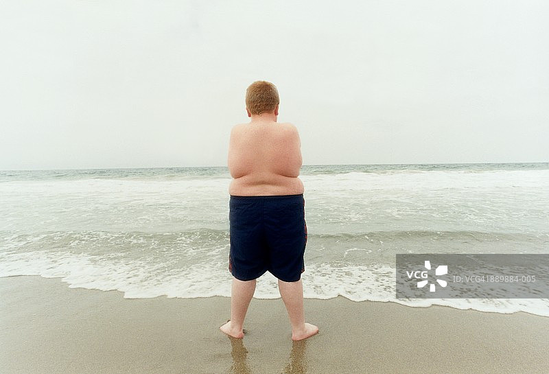 站在海滩上的超重男孩（10-12岁），后视图图片素材
