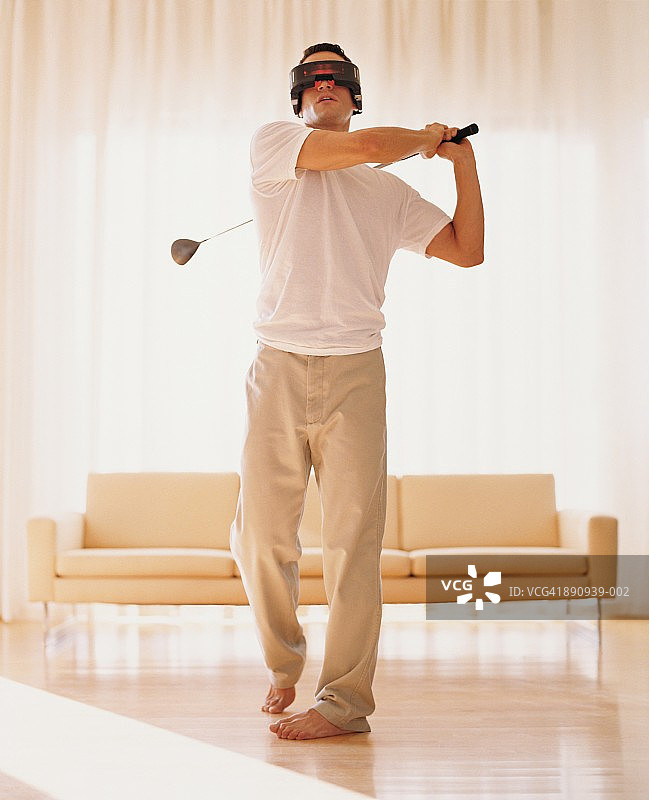 戴着VR眼镜在家打高尔夫的年轻人图片素材