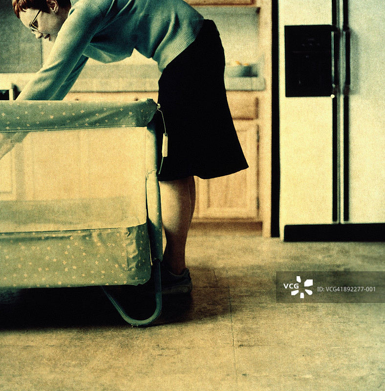 在厨房里的年轻女人，伸手进入婴儿床（纸底片）图片素材