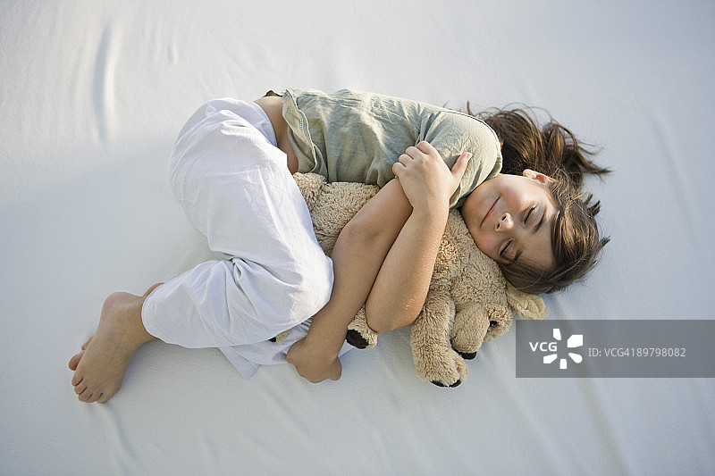 女孩抱着泰迪熊睡觉的俯视角度照片图片素材