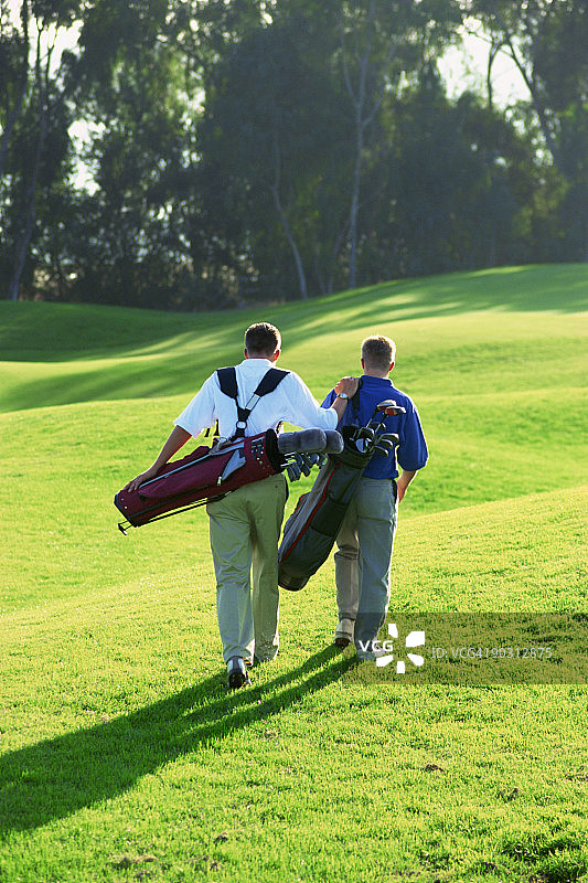 父子带着高尔夫球袋在球场上图片素材