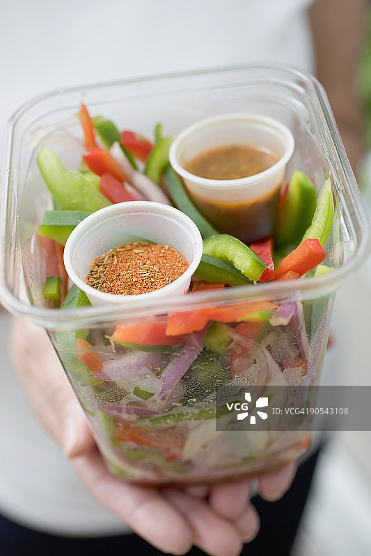 手拿蔬菜、调味品和蘸料塑料容器的女人（局部特写）图片素材