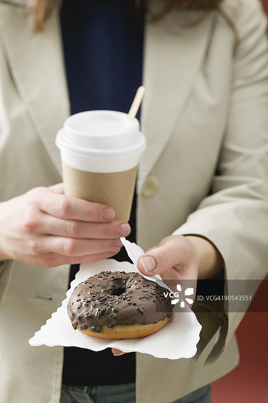 手持巧克力甜甜圈和咖啡杯的女人特写图片素材