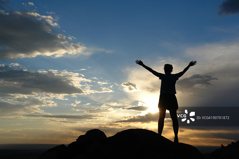 日落天空背景下举起双臂的女性剪影图片素材