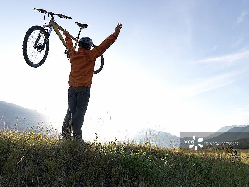 山地自行车手在山脊上举起自行车图片素材