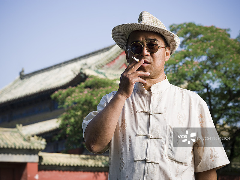 戴墨镜和帽子的中国男人吸烟图片素材