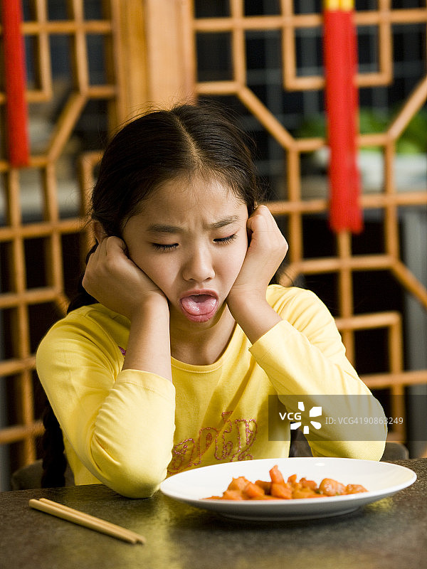 女孩坐在桌旁厌恶地看着盘中食物图片素材