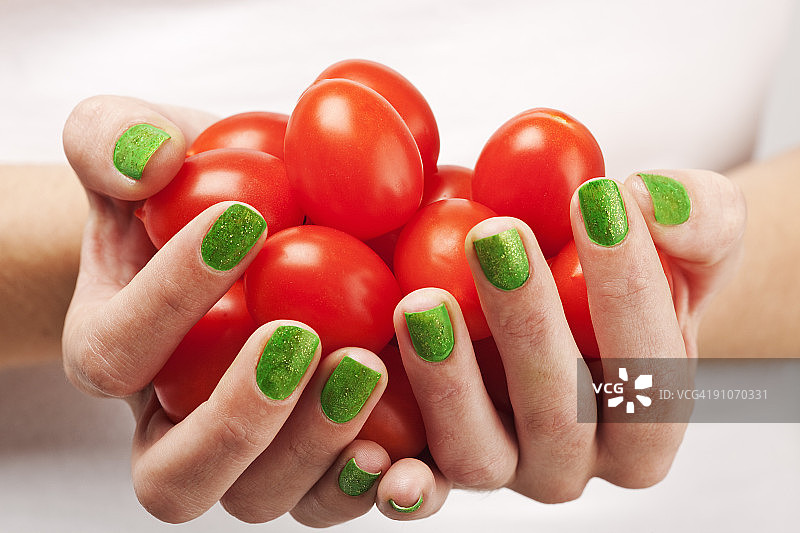 涂有绿色指甲油的手拿着西红柿图片素材