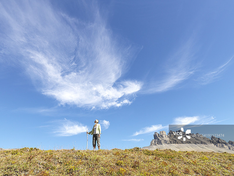 女人手持登山杖站在大型山地草甸上图片素材
