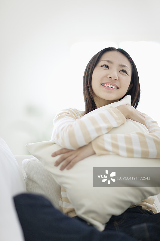女人坐在沙发上，抱着靠垫微笑图片素材