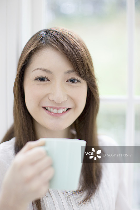 手捧马克杯微笑的年轻女人肖像图片素材