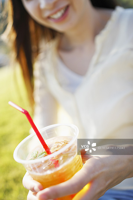 坐在田野里，拿着冷饮的女人（中部视角）图片素材