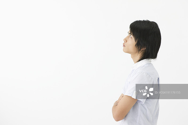 手臂交叉向上看的年轻男人，侧视图，工作室照片图片素材